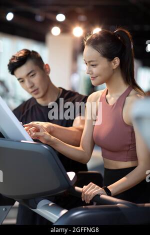 Junge Frau, die im Fitnessstudio mit Personal Trainer trainiert Stockfoto