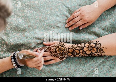 Künstlerin, die Henna-Tätowierung auf Frauenhänden anwendet. Mehndi ist traditionelle indische dekorative Kunst, Hand mit floralen Mehendi. Beauty-Zeichnung für Hochzeiten und Stockfoto