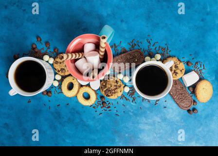 Tassen Kaffee und verschiedene Kekse und Sümpfe auf blauem Hintergrund. Essen und Trinken, Draufsicht flach liegend. Stockfoto