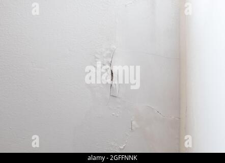 Die weiße Wand blättert ab und ein langer Riss in der Nähe der Ecke des Schlafzimmers, Regen und Feuchtigkeit aus der Regenzeit sickern aus rissigen Fenstern Stockfoto