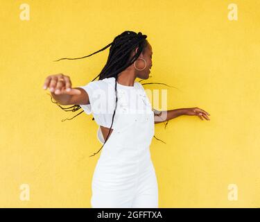 Junge Frau in weiß insgesamt Spaß an einer gelben Wand im Freien Stockfoto