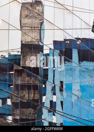 Iquitos, Peru - Dez,2019: Das verlassene, unvollendete, blaue Gebäude spiegelt sich im Glas eines modernen Wolkenkratzers wider. Amazonien, Lateinamerika. Stockfoto