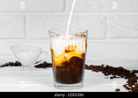 Milch wird in Eiskaffee auf weißem Hintergrund gegossen, Erfrischungsgetränk im Sommer, Kaffeebohne, Copyspace Stockfoto