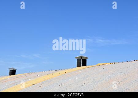 Belüftungssystem auf dem Blechdach des industriellen Fabrikschuppens. Blauer Himmel. Stockfoto