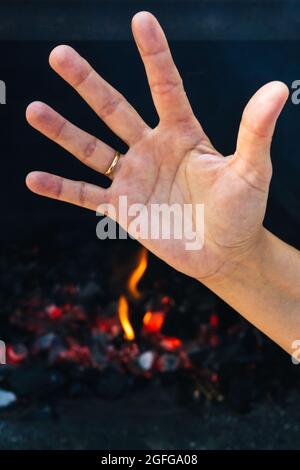 Detail einer Hand mit der Stop-Geste bei der Vorbereitung eines Feuers für ein Barbecue an einem windigen und sonnigen Tag mit selektivem Brandgefahrenkonzept Stockfoto