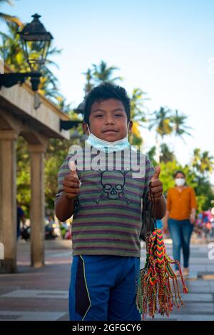 Ryohacha, La Guajira, Kolumbien - Mai 26 2021: Porträt eines Wayuu-Jungen in einem gestreifte T-Shirt, trägt eine Maske unter seinem Mund und schaut auf das C Stockfoto