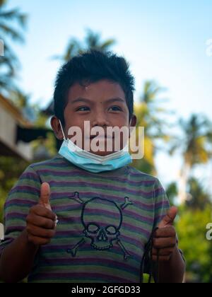 Ryohacha, La Guajira, Kolumbien - Mai 26 2021: Porträt eines Wayuu-Jungen in einem gestreifte T-Shirt, trägt eine Maske unter seinem Mund und schaut auf das C Stockfoto