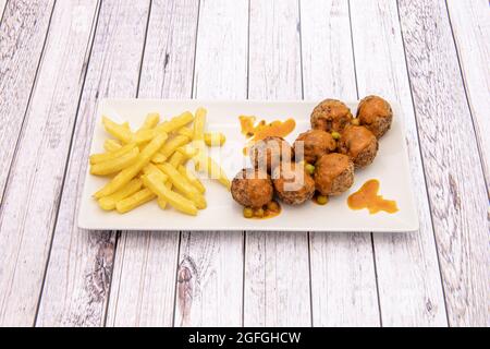 Fleischbällchen in Soße, garniert mit Kartoffeln und Erbsen in weißem Teller auf weißem Holztisch Stockfoto