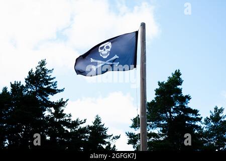 Schwarze Totenkopf-Piratenflagge winkt im Wind am blauen Himmel. Stockfoto