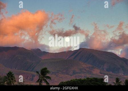 Vollmond, der bei Sonnenuntergang über den Bergen von west maui aufgeht, mit rosa geschwollenen Wolken. Stockfoto