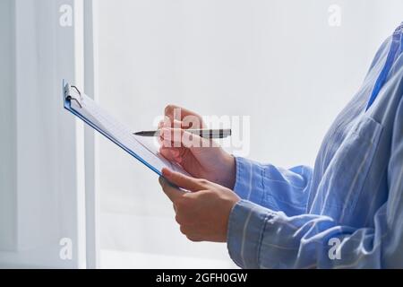 Seitenansicht einer nicht erkennbaren Frau in formeller Kleidung, die mit einem Stift auf der Zwischenablage Notizen gemacht hat Stockfoto