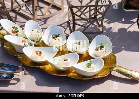 Snacks in weißen Schalen auf einem goldenen Teller in Form des Baumblattes Stockfoto