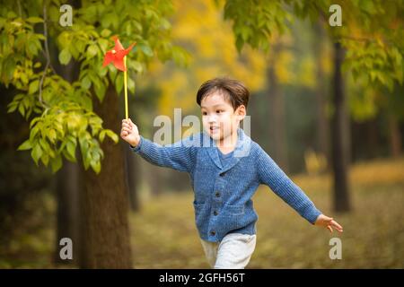 Kleiner Junge, der mit Papierwindmühle im Wald spielt Stockfoto