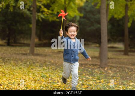 Kleiner Junge, der mit Papierwindmühle im Wald spielt Stockfoto