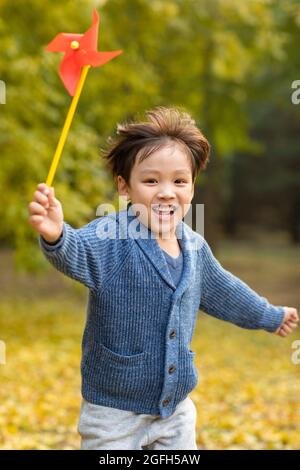 Kleiner Junge, der mit Papierwindmühle im Wald spielt Stockfoto