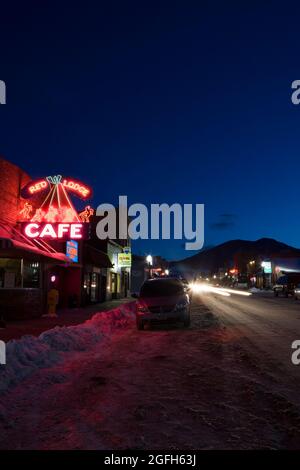 Neonschilder leuchten, Scheinwerfer und Rücklichter leuchten, und der Horizont verfärbt sich von Blau zu Schwarz, wenn die Winternacht in Red Lodge, MT, einbricht. Stockfoto