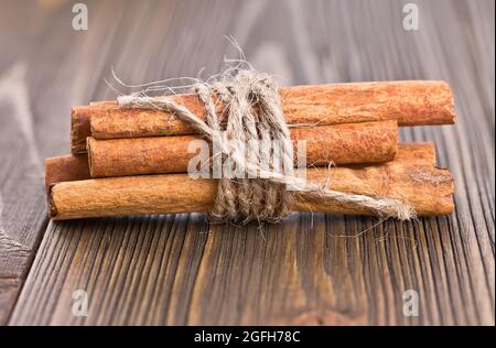 Einige Zimtstangen, die mit Garn auf einem alten Holzbrett gebunden sind Stockfoto