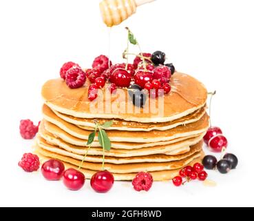 Stapel von Pfannkuchen mit Beeren und Honig isoliert auf weißem Hintergrund Stockfoto