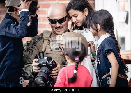 Kabul, Afghanistan. August 2021. Eine US-Marine, die der 24. Marine Expeditionary Unit zugeordnet ist, zeigt ihre Kamera Kindern, die auf die Evakuierung warten, am Hamid Karzai International Airport, Afghanistan, 24. August 2021. Die USA unterstützen das Außenministerium bei einer nicht-kombatanten Evakuierungsoperation (NEO) in Afghanistan. Foto von Melissa Marnell/US Marine Corps via CNP/ABACAPRESS.COM Quelle: Abaca Press/Alamy Live News Stockfoto