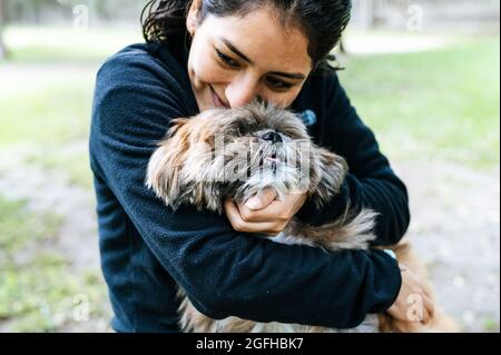 Nette junge Frau küsst und umarmt ihren kleinen Welpen. Liebe zwischen Besitzer und Hund. Außenfoto im Park, selektiver Fokus. Lifestyle-Konzept Stockfoto