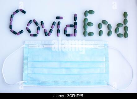 Inschrift Covid Ende von farbigen Tabletten mit medizinischer Maske Stockfoto