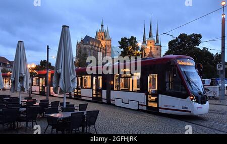 Erfurt, Deutschland. August 2021. Am frühen Morgen fährt eine Straßenbahn an einer Kneipe mit gefalteten Sonnenschirmen auf dem Domplatz vorbei. Im Hintergrund ist die St. Mary's Cathedral und die Severi Kirche zu sehen. Am Donnerstag ist es in vielen Teilen Thüringens bewölkt, es sind Duschen möglich. Quelle: Martin Schutt/dpa-Zentralbild/dpa/Alamy Live News Stockfoto