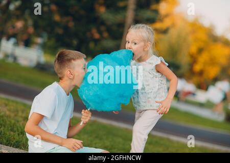 Glückliche Kinder Junge und Mädchen essen blaue Zuckerwatte im Freien. Stockfoto