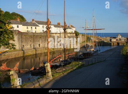 Bemalte Hütten und hohe Schiffe kurz vor Sonnenuntergang im Hafen von Charlestown, Cornwall, England Stockfoto