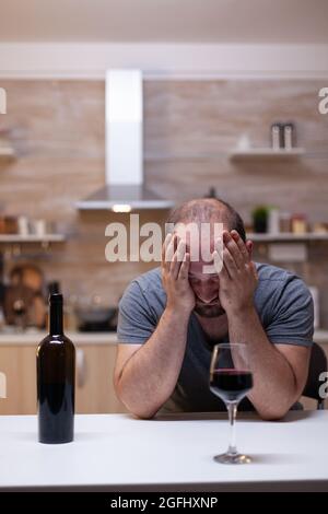 Verzweifelter Mann, der sich unglücklich fühlte, als er allein Glas mit Wein und Flasche trank. Person mit ungesunder sucht sitzt mit Alkohol, Alkohol, alkoholisches Getränk verärgert Stockfoto