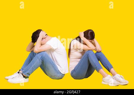 Gestresst Junges Paar, das sich zurück zu Rücken sitzt.Kopf halten.Selbstschutz. Isoliert auf gelbem Hintergrund. Stockfoto