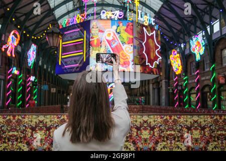 London UK 26. August 2021 EIN Besucherfoto Covent Garden „Do you See words in Rainbows“ eine neue immersive großformatige Kunstinstallation der britischen Künstlerin Chila Burman. Burmas riesige Neonskulpturen verwandeln den Raum in ein riesiges Neon-Wunderland voller erhebender Botschaften für Besucher. In Neonviolett über dem ikonischen Eingang der South Hall prangt Paul Quezada-Neiman/Alamy Live News Stockfoto