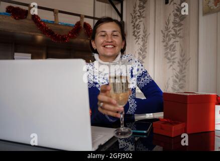 Glückliche asiatische Frau trägt blauen Pullover mit einem Glas Champagner, im Gespräch mit der Familie, soziale Distanz Freund von Videokonferenz Gespräch Gespräch ein Stockfoto