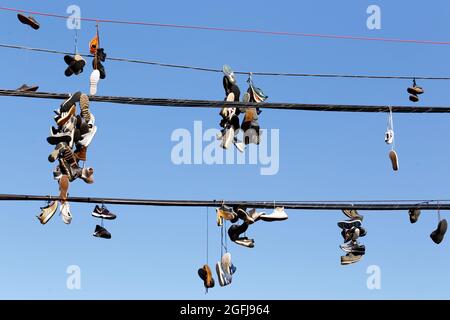 Shoeffiti, Sneakers, die am Telefonkabel an einem sonnigen blauen Himmel hängen; Sneakers, die zusammengebunden sind und über eine Stromleitung geschleudert werden.