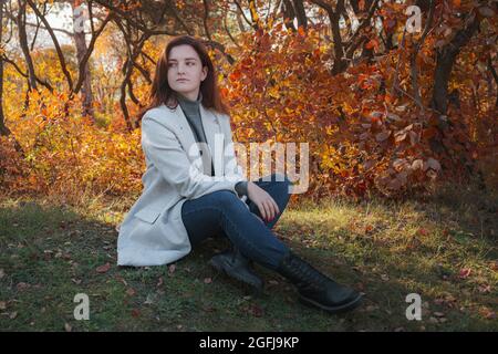 Eine niedliche rothaarige Frau in guter Laune posiert an einem Herbsttag und genießt das schöne Wetter. Das Konzept und die Idee, Herbst und Herbst Getaway zu genießen Stockfoto