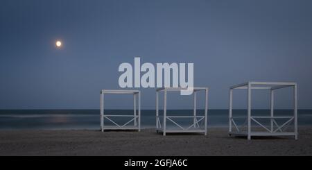 Drei hölzerne Pavillons auf Sand, Meer und Mond bei Nacht Stockfoto