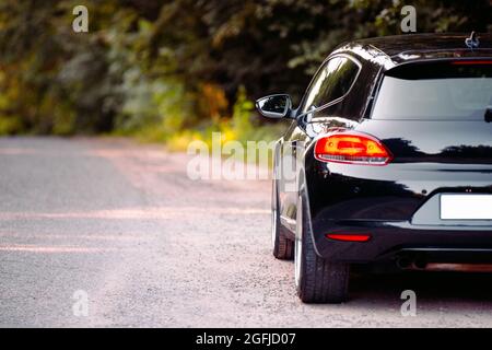 Rückansicht Foto einer schwarzen Limousine-Marke mit der Haltestelle auf der Straße in der Nähe des Waldes. Stockfoto