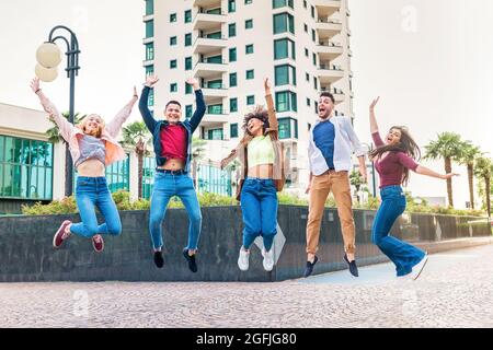 Eine Gruppe ausgelassener, vielfältiger junger Freunde, die in der Luft in einer Stadtstraße springen und vor Freude jubeln und lachen, während sie gemeinsam feiern Stockfoto