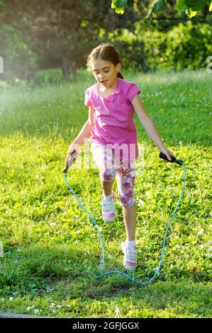 Fröhliches, energiegeladenes junges Mädchen, das im Frühjahr oder Sommer ein Springseil in einem üppigen grünen Garten in einem gesunden, aktiven Outdoor-Lifestyle-Konzept verwendet Stockfoto