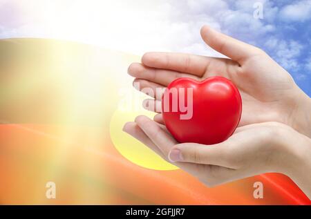 Kinderhände halten ein Herz auf dem Hintergrund der Flagge der australischen Aborigines, Gesundheitskonzept. Stockfoto