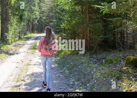 Ein junges Mädchen mit Rucksack zu Fuß entlang Weg durch den Wald während des Sommers. Hipster Lifestyle und Solo Trip.Rückansicht. Stockfoto