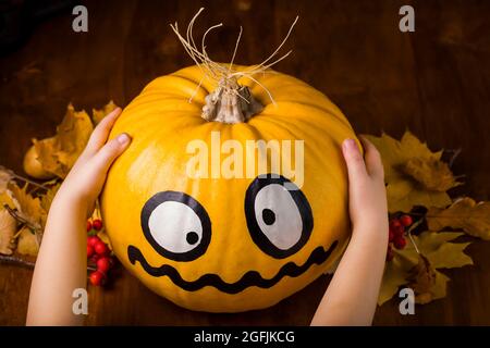 Einfache Kürbis-Basteln für Kinder. Mache Kürbis-Deko für Halloween. Kürbis in den Händen auf dunklem Holzhintergrund Stockfoto