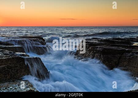 Farbenprächtiger Sonnenaufgang über dem pazifischen Ozeanhorizont vor dem Strand Narrabeen, Sandsteinfelsen an der Küste und der Küste der nördlichen Strände von Sydney. Stockfoto