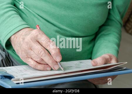 Nahaufnahme faltige Hand einer älteren Person, die zu Hause Kreuzworträtsel macht Stockfoto