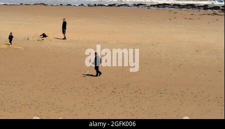 WHITLEY BAY. TYNE und WEAR. ENGLAND. 05-27-21. Der Strand mit einem Mann, der einen Metalldetektor benutzt. Es gibt auch eine Familiengruppe. Die Flut beginnt sich zu wenden Stockfoto