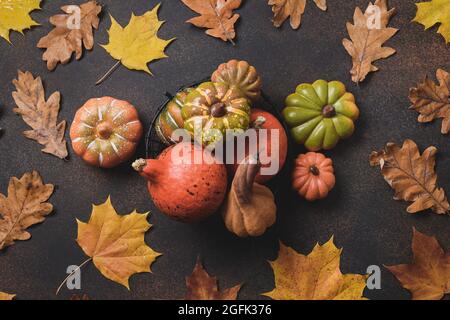 Kürbisse und bunte trockene Herbstblätter auf braunem Hintergrund. Herbstkomposition. Draufsicht. Erntedankfest. Flach liegend. Stockfoto