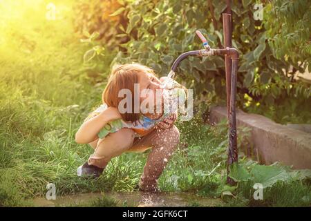 Nettes Mädchen, das Wasser aus dem Wasserhahn auf dem Land trinkt Stockfoto