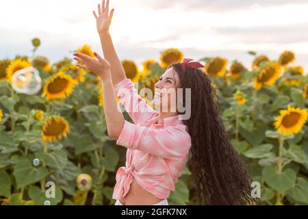 Nette Brünette Frau bläst Seifenblasen. Schönes Feld mit Sonnenblumen auf dem Hintergrund. Stockfoto