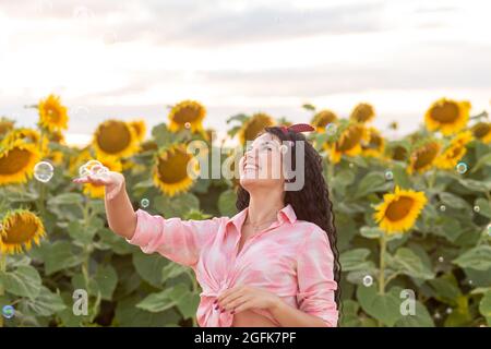 Nette Brünette Frau bläst Seifenblasen. Schönes Feld mit Sonnenblumen auf dem Hintergrund. Stockfoto