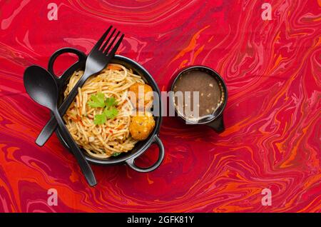 Veg Schezwan Hakka Noodles serviert in einer schwarzen Schüssel mit Manchow-Suppe auf rotem Hintergrund Stockfoto