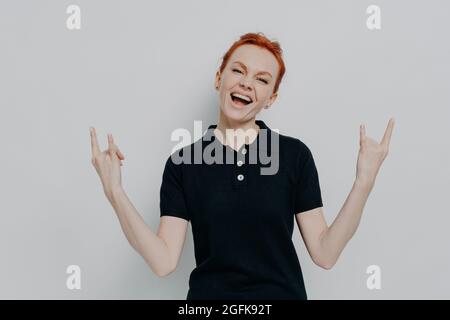 Energisch verrückte junge Frau mit roten Haaren, die Hände in Rock and Roll-Zeichen hält und schreit Stockfoto